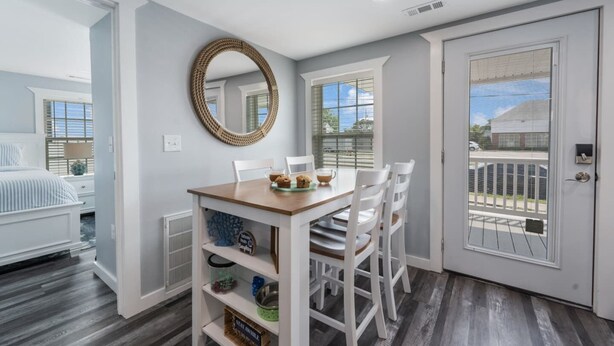 A dining area with a wooden table, white chairs, a woven mirror, and a view of the outside through a door. - 4 Seat Golf Cart~Family Friendly~Near DT Beaufort! (Beaufort)