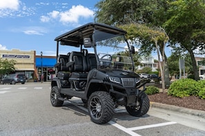 Un carro de golf negro estacionado en una calle, con un edificio que dice "Island proper" al fondo.