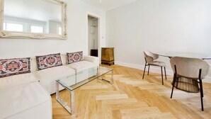 En moderne stue med et glasbord, hvid sofa og et stort spejl.