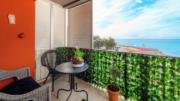 A balcony with a wicker chair, a small table with a potted plant, and a view of the sea.