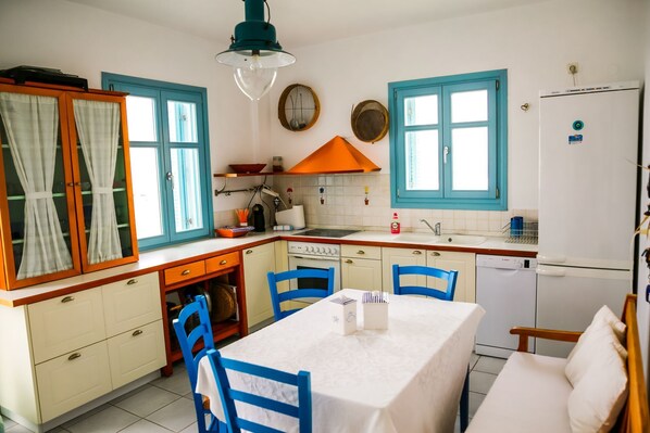 A compact kitchen with a dining area, featuring a stove, sink, and refrigerator. - 360 Blue (Santorini)
