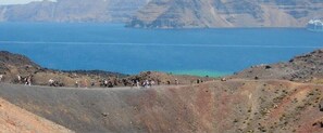 A rocky landscape with a group of people gathered at the edge of a cliff overlooking a calm sea. - 360 Blue (Santorini)
