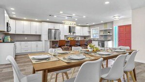 A modern kitchen with white cabinets, a wooden dining table set for four, and a red door in the background.
