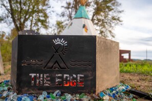 A metal sign with a mountain and sun design, labeled 'THE EDGE.' - The Dreamcatcher Teepee at The Edge—Unique Riverfront Glamping in Salt Lick, KY (Salt Lick)