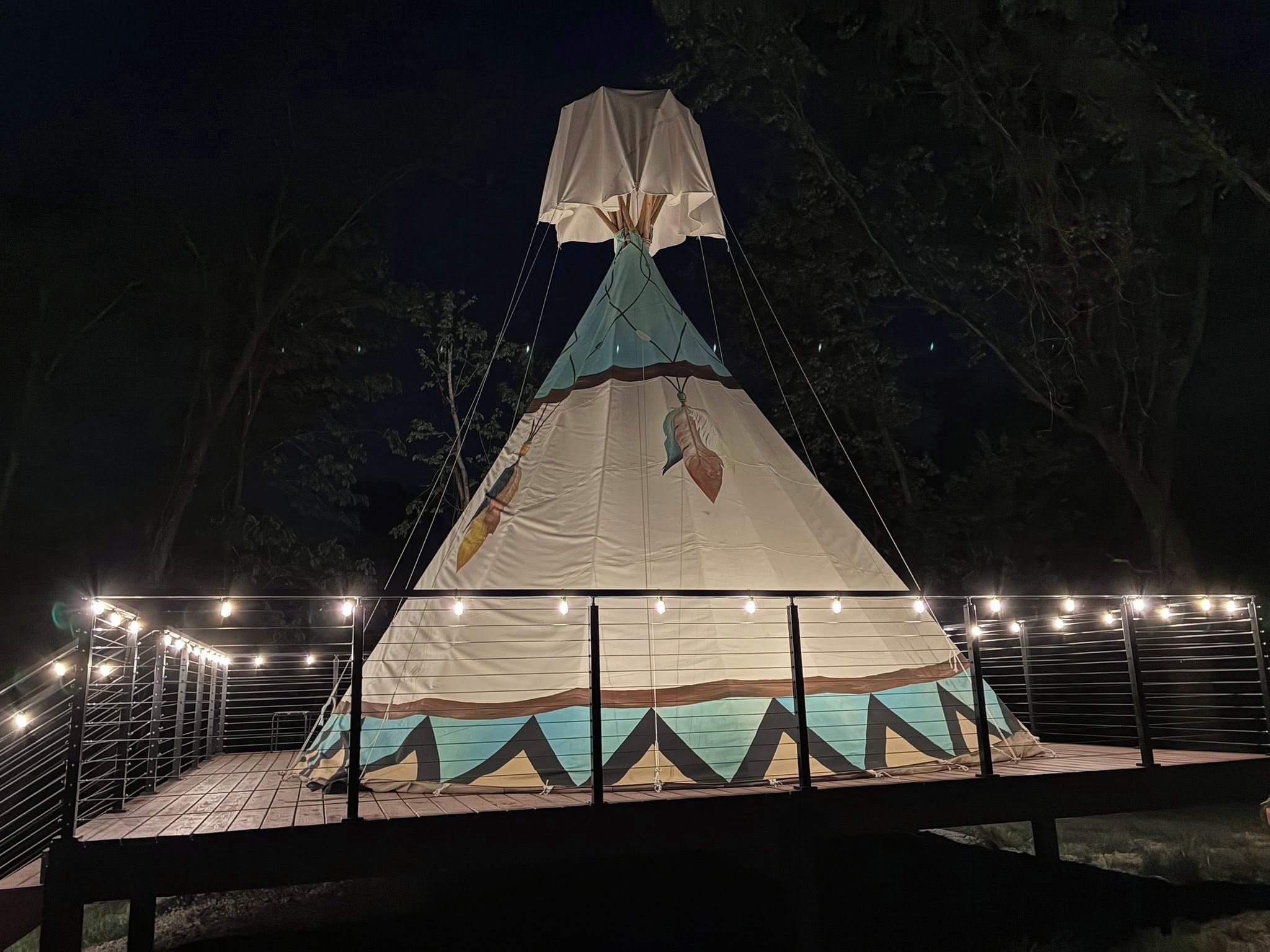 A large, white, pyramid-shaped tent with a hanging decoration, surrounded by a metal railing and string lights.