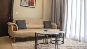 A living room with a beige sofa, two dark cushions, a small round coffee table, and a framed picture on the wall. - The Bravia Residency by Cozy (Accra)