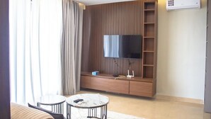 A modern living room with a flat-screen TV mounted on a wooden wall, a sofa, two small tables, and a built-in shelf. - The Bravia Residency by Cozy (Accra)