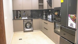 A compact kitchen with a dishwasher, oven, and refrigerator. - The Bravia Residency by Cozy (Accra)