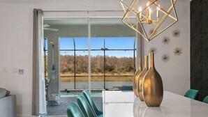 Ein moderner Essbereich mit Glastür und Seeblick, einem weißen Tisch und grünen Stühlen.