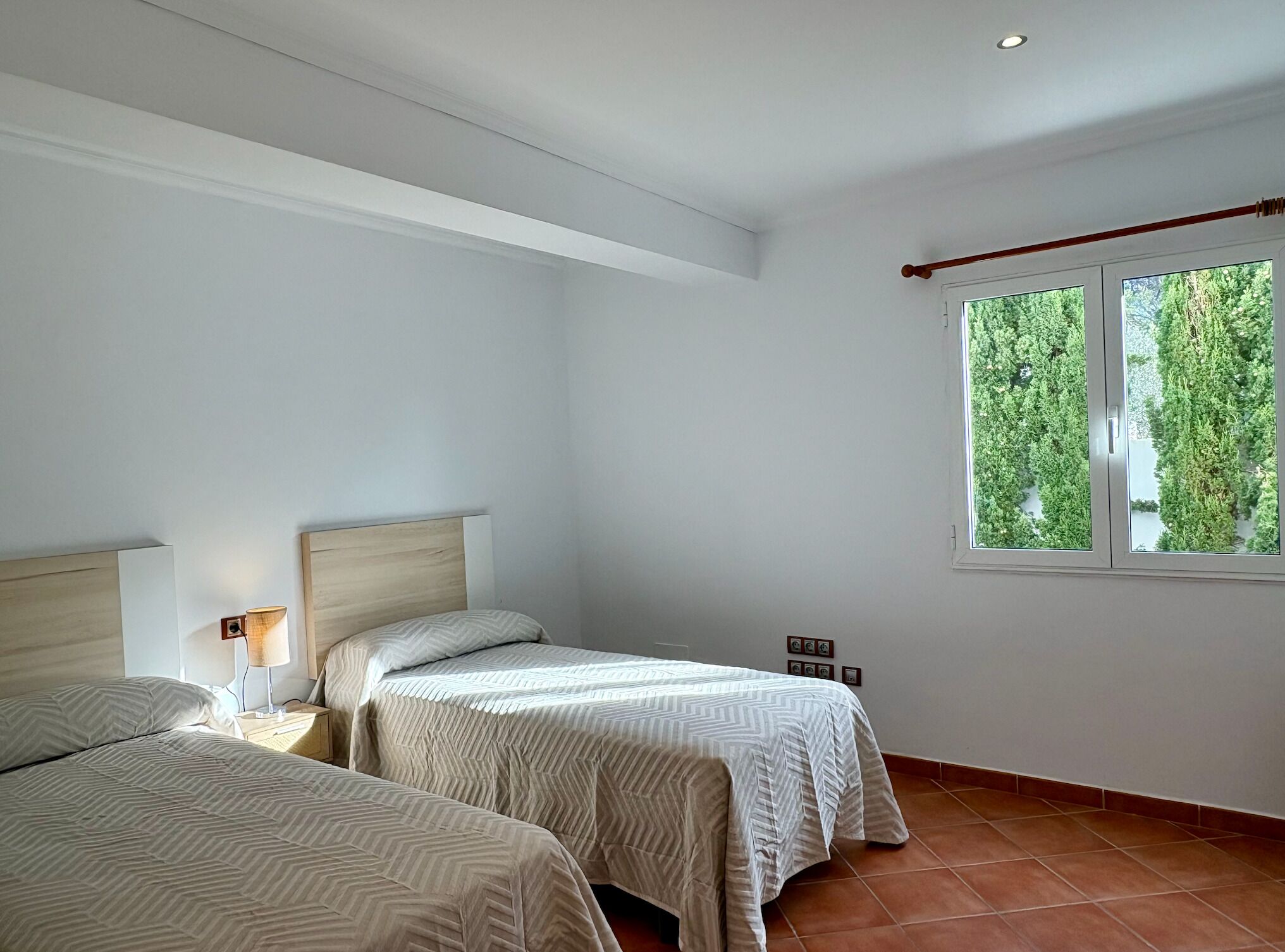 Un dormitorio con dos camas, una ventana que da a zonas verdes y un cabecero de madera.