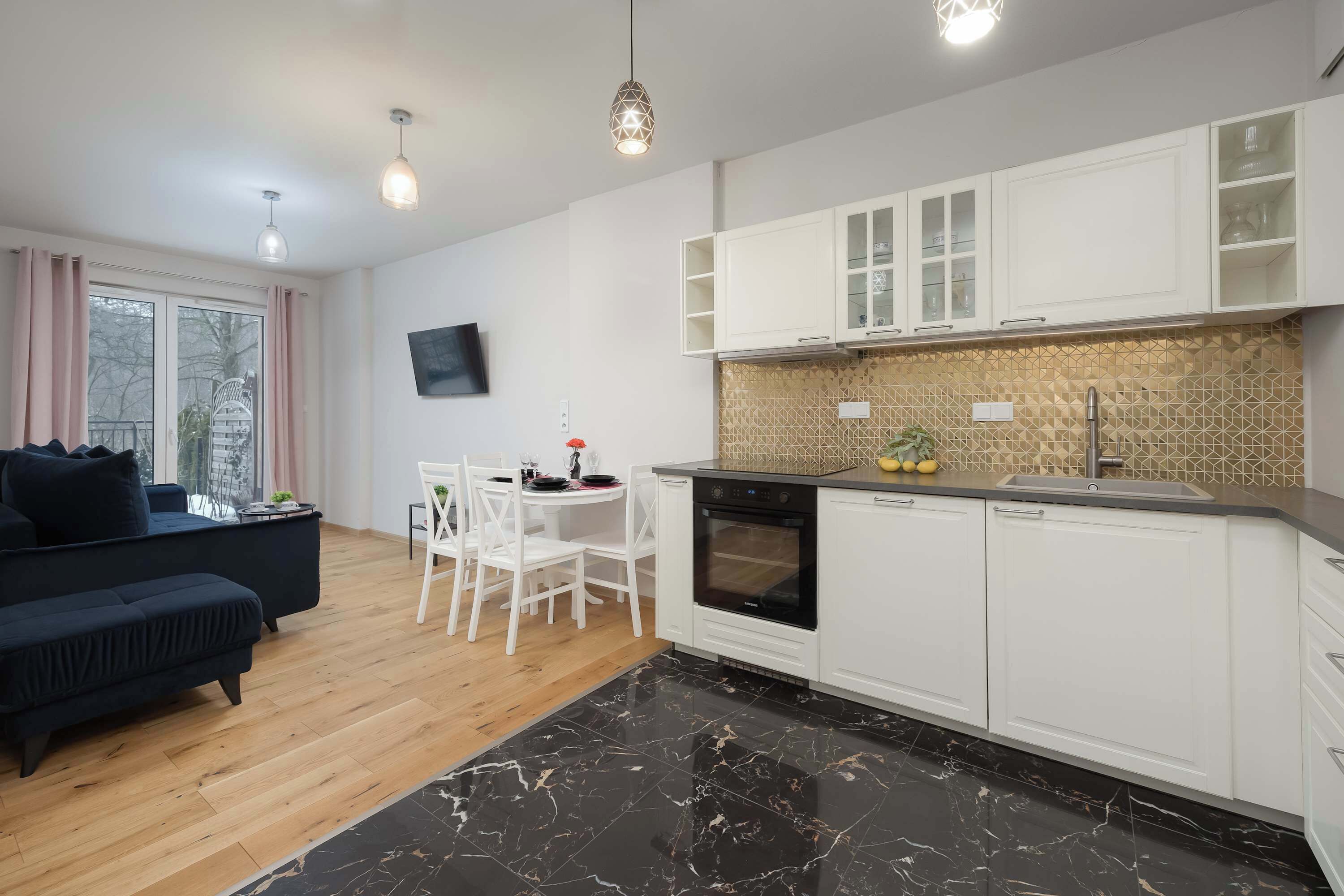 A modern kitchen with white cabinets, a black marble countertop, and a dining area with a white table and chairs.