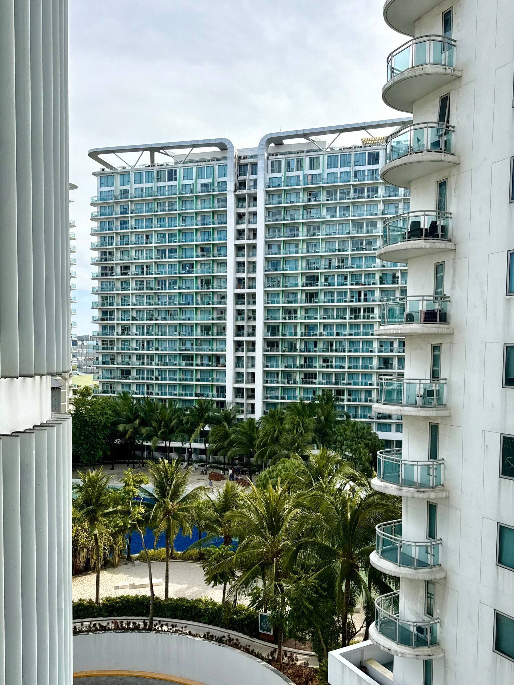 A high-rise hotel with multiple balconies, a beach view, and palm trees.