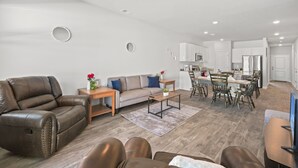 A modern living room with a leather sofa, a beige sofa, and a dining area with wooden chairs and a table. - New Modern 3BR/3BA Townhome. Quiet Retreat w/Pool, Playground and Free Parking. (Conway)