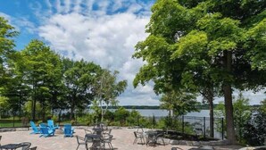 Un patio al aire libre con mesas y sillas, rodeado de árboles y vista a un lago.
