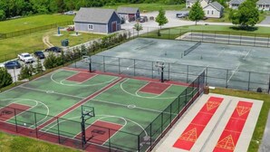 Una cancha de baloncesto al aire libre con varias canchas, un área cercada y un estacionamiento.