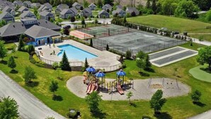 Un barrio residencial con casas, piscina, parque infantil y cancha de tenis.