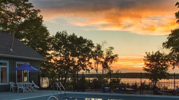 Piscina con vista al atardecer, rodeada de árboles y una valla.