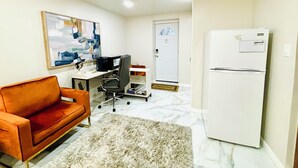 Un espacio habitable compacto con un sofá, un escritorio con computadora, un refrigerador y una puerta.