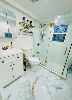 A modern bathroom with a glass-enclosed shower, white marble flooring, and a white toilet.