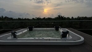 Een hottub met vier stoelen op een houten terras, omgeven door een leuning, met een zonsondergang op de achtergrond.