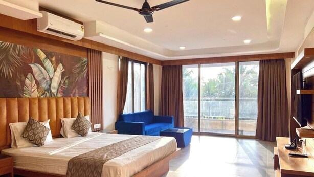 Een moderne hotelkamer met een groot bed, een blauwe bank, een flatscreen-tv en een balkon met uitzicht.