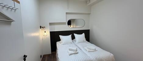 A neatly made bed with white bedding, a bedside lamp, and a mirror above it.