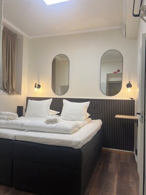 A neatly made bed with white linens, two wall-mounted mirrors, and a bedside table with a lamp. - Oxbackens Hotell & cafe (Västerås)