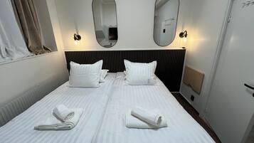 A hotel room with a large bed, two white pillows, two white towels, a black headboard, and two wall-mounted mirrors.