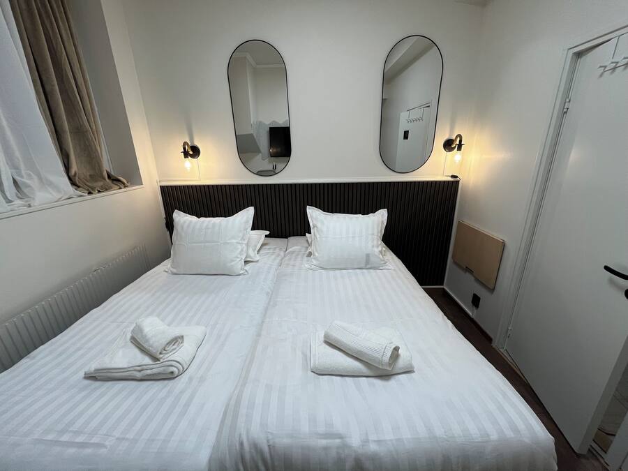 A hotel room with a large bed, two white pillows, two white towels, a black headboard, and two wall-mounted mirrors.