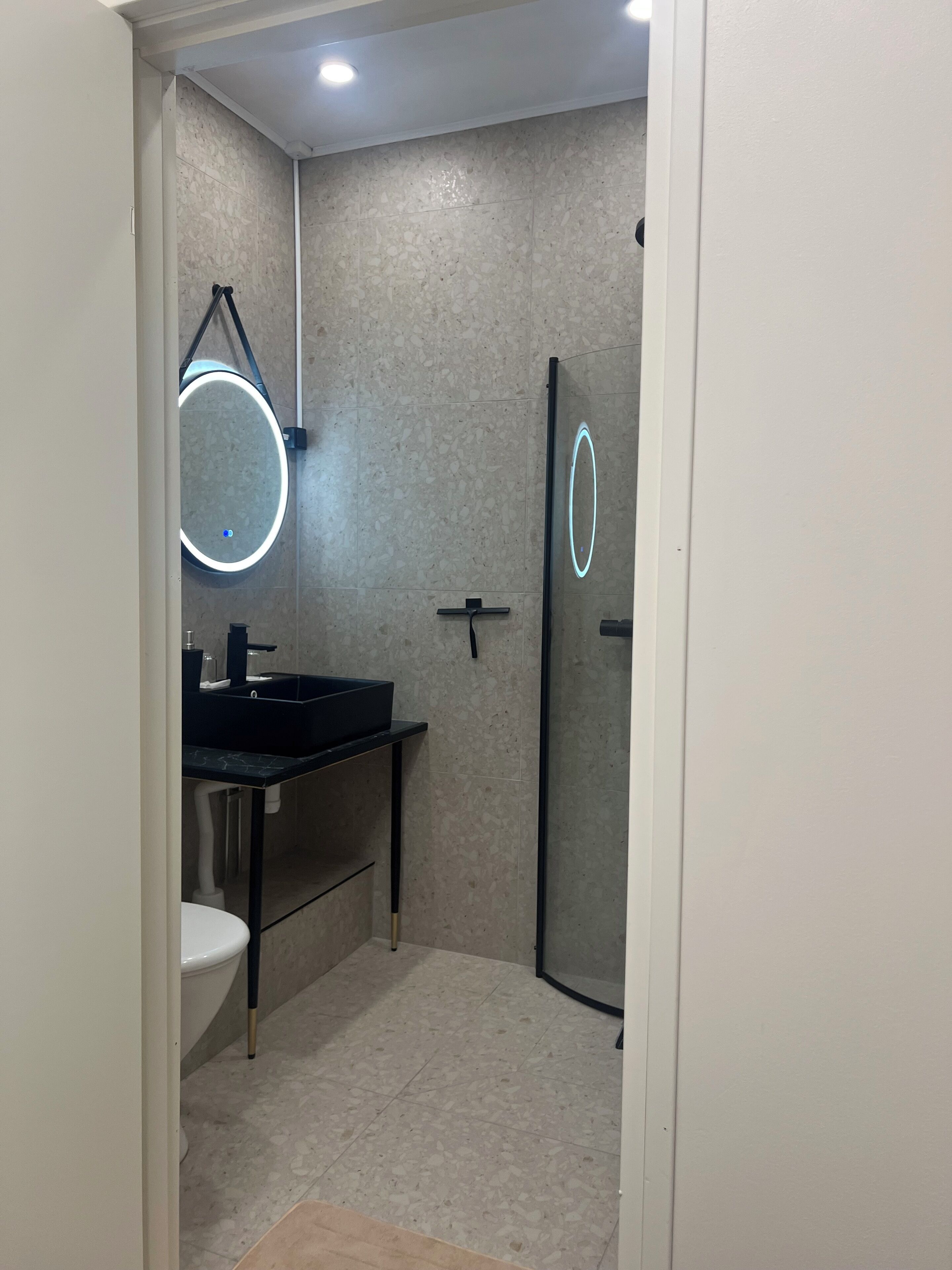 Un bany modern amb un mirall rodó, un lavabo negre i una cabina de dutxa de vidre.