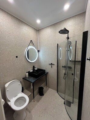 A modern bathroom with a toilet, sink, and glass-enclosed shower. - Oxbackens Hotell & cafe (Västerås)