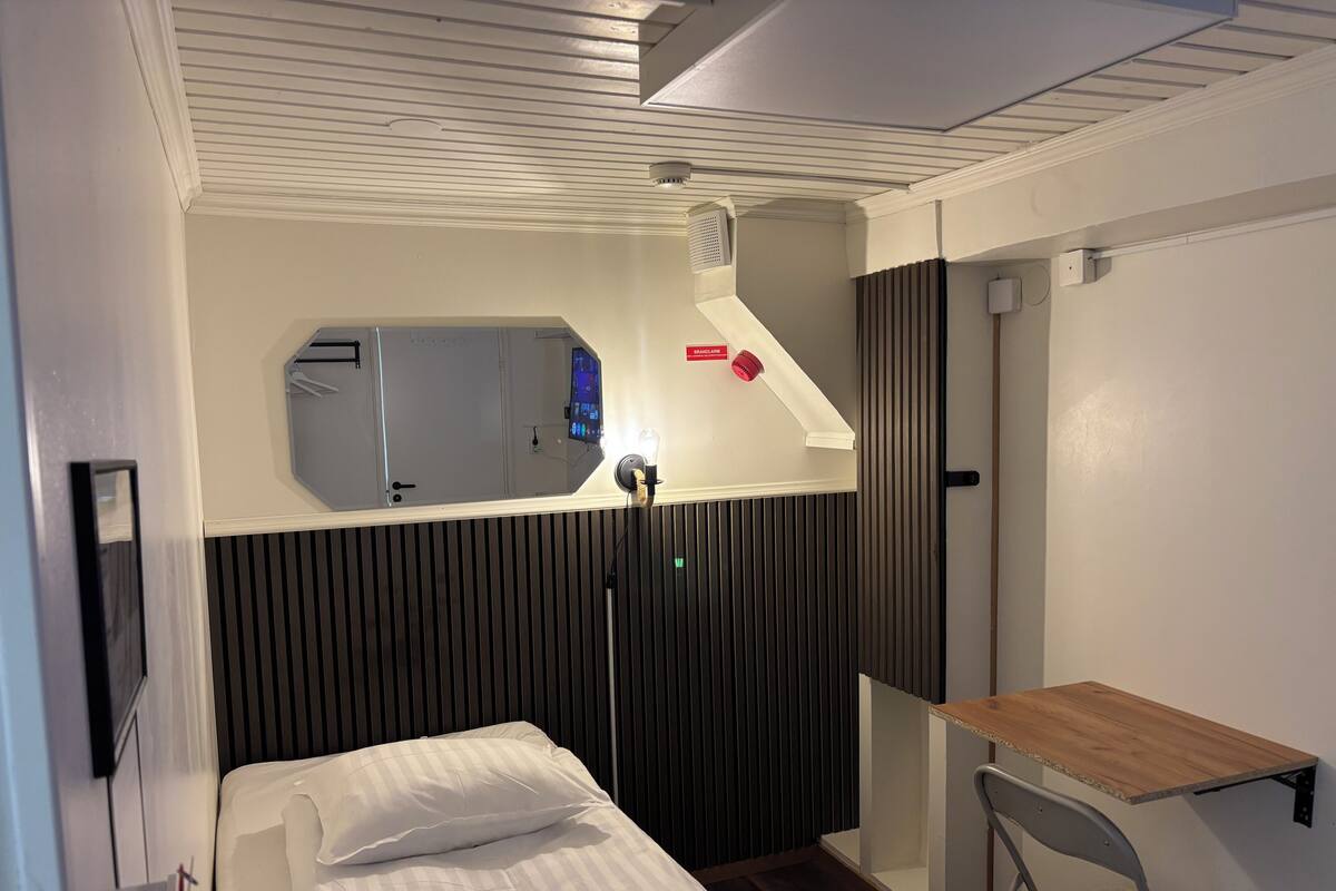 Ein Hotelzimmer mit einem Bett, einem Nachttisch, einem Spiegel, einer Lüftung und einer Tür.