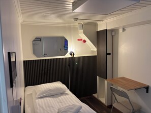 A hotel room with a bed, a bedside table, a mirror, a vent, and a door. - Oxbackens Hotell & cafe (Västerås)