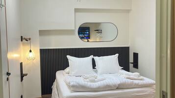 Un dormitorio con cama, un espejo en la pared, una mesita de noche y una lámpara de pared.