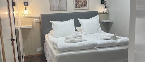 A neatly made bed with white linens and pillows, a gray headboard, and two wall-mounted pictures.
