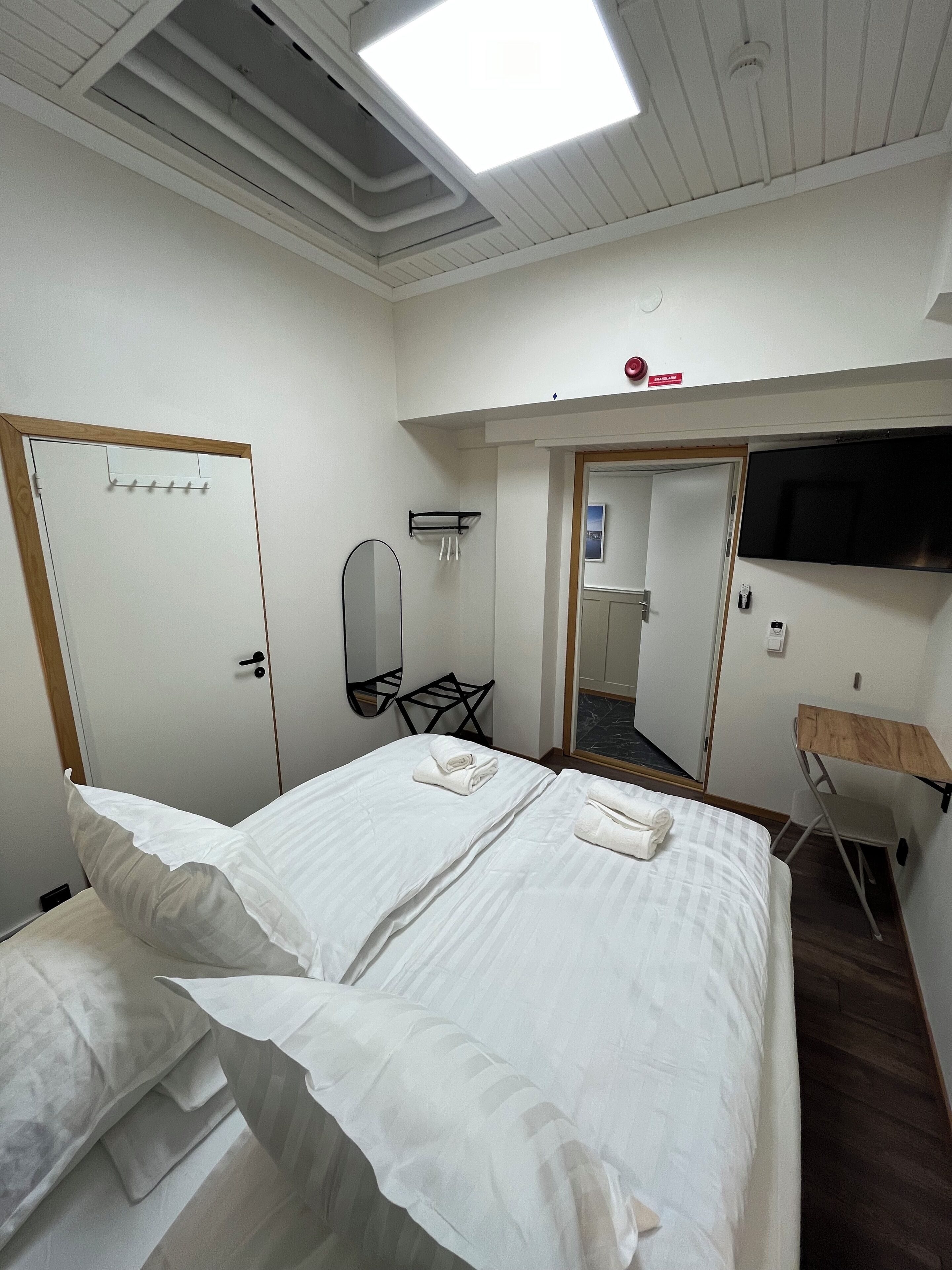 Ett hotellrum med två sängar, en platt-TV som är monterad på väggen, ett litet skrivbord och en spegel.