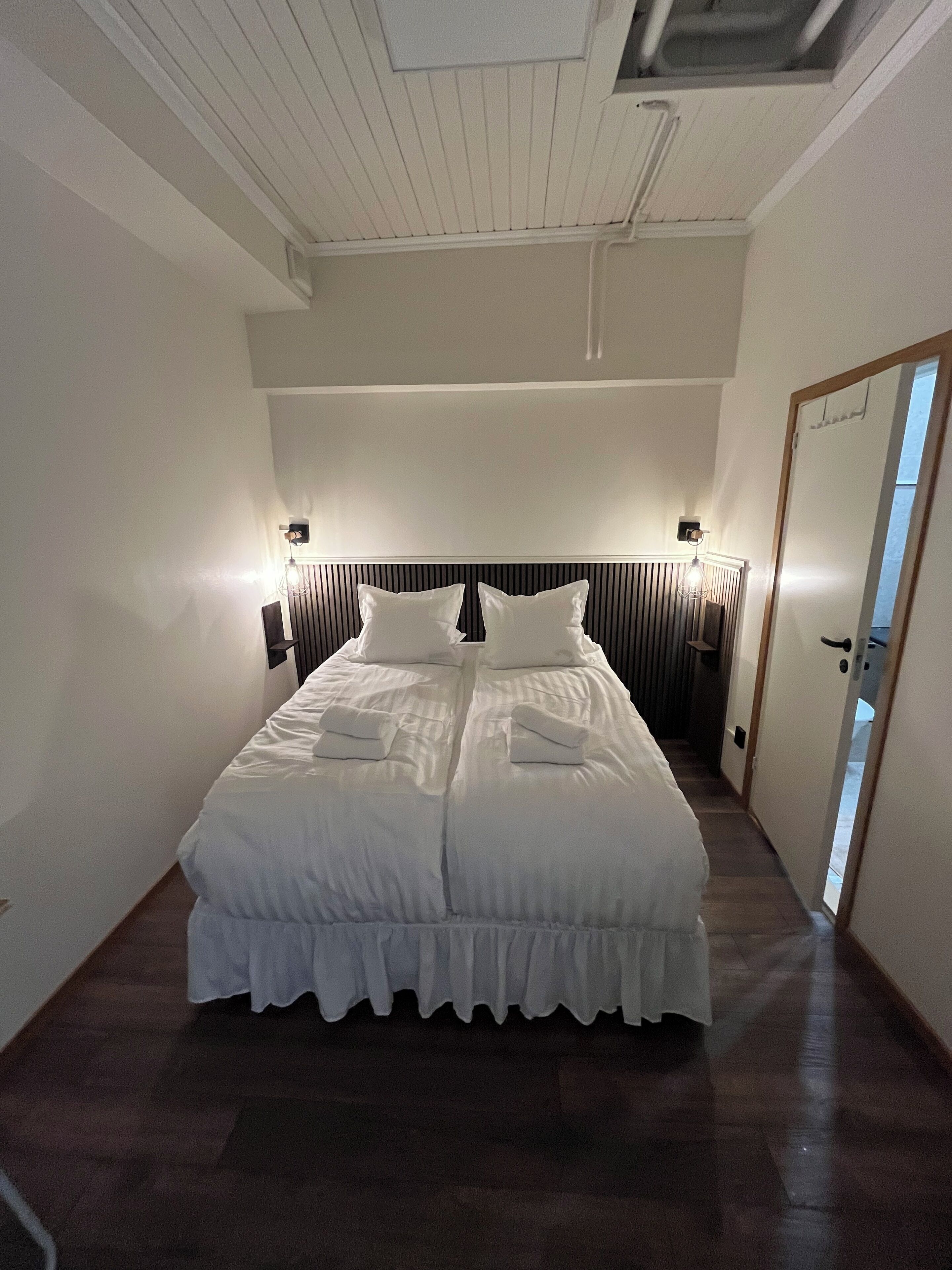A neatly made bed in a hotel room with a headboard, two bedside lamps, and a door to the right.