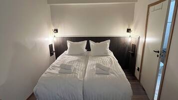 A neatly made bed in a hotel room with a headboard, two bedside lamps, and a door to the right.