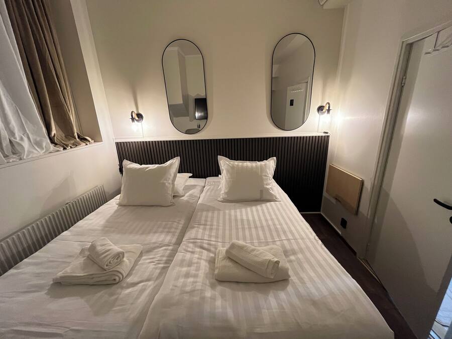 Hotellihuone, jossa on suuri sänky, kaksi seinäpeiliä ja ikkuna, jossa on verhot.