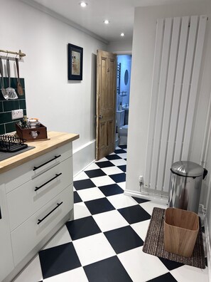 Una cocina moderna con piso a cuadros, armarios blancos y una puerta de madera que da a un baño.