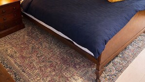 Un dormitorio con cama de madera, paredes verdes, alfombra estampada y radiador blanco.