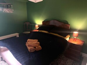 Una cama con toallas enrolladas, una mesita de noche con lámpara y un cabecero de madera.