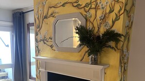 Una habitación con chimenea, un espejo encima y un mural floral en la pared.
