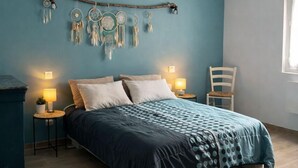 Een slaapkamer met een bed, nachtkastjes, een stoel, een dromenvanger en een raam.