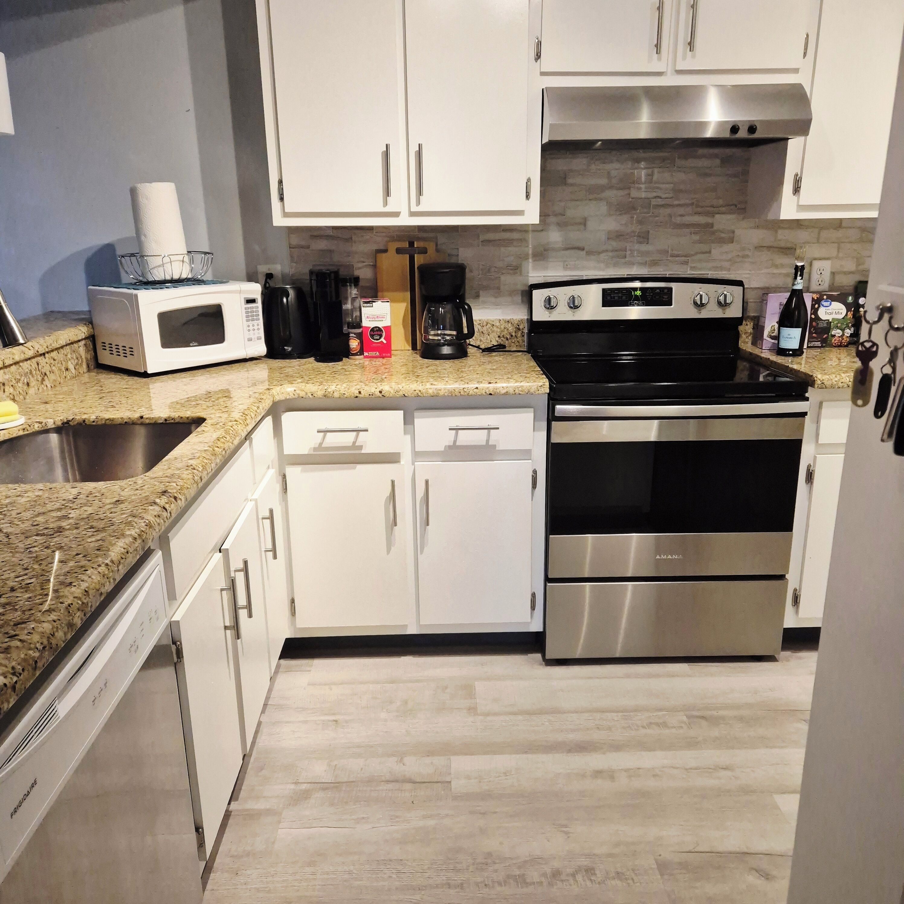 A modern kitchen with stainless steel appliances, white cabinetry, and a granite countertop.
