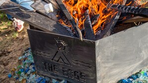 A metal fire pit with a logo, surrounded by fire and wood. - Naut on Call Geodome at The Edge—Unique Riverfront Glamping in Salt Lick, KY (Salt Lick)