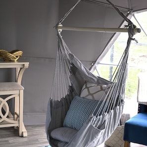 A hanging chair with a grey and white fabric, a patterned pillow, and a wooden table with a woven basket.
