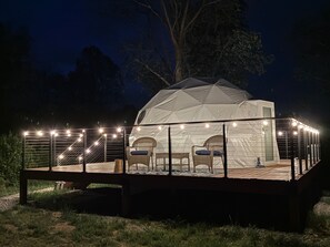 A dome-shaped tent with a covered deck and string lights.