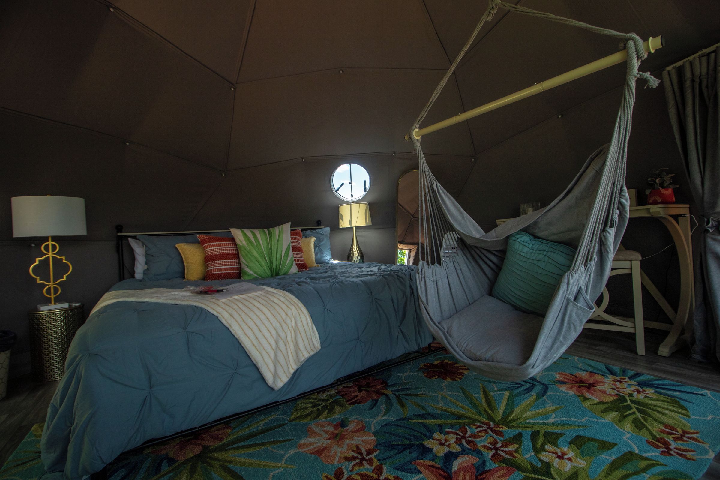 Una habitación con una cama, una silla colgante, una lámpara y una ventana.