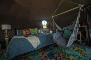 A room with a bed, a hanging chair, a lamp, and a window.